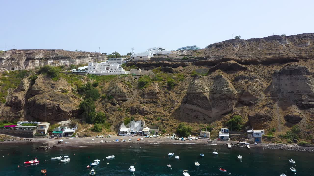 vista estática aérea de la isla griega, acantilado rocoso con villas y barcos de pesca en el mar mediterráneo en la playa de santorini, grecia