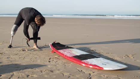 Totale-Eines-Männlichen-Surfers-Mit-Beinprothese,-Der-Den-Surfbrettgurt-Anlegt