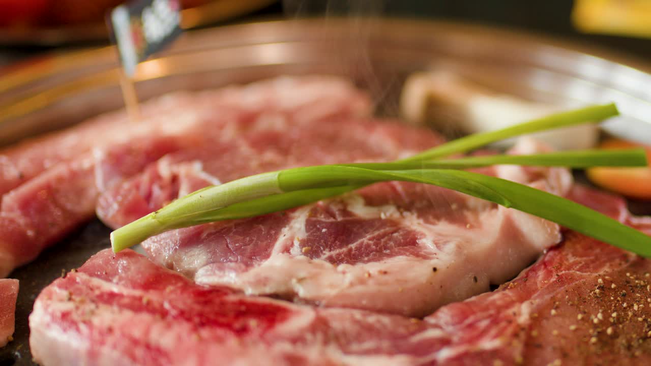 Close-up of raw beef, green onions, and vegetables sizzling on a hot grill pan