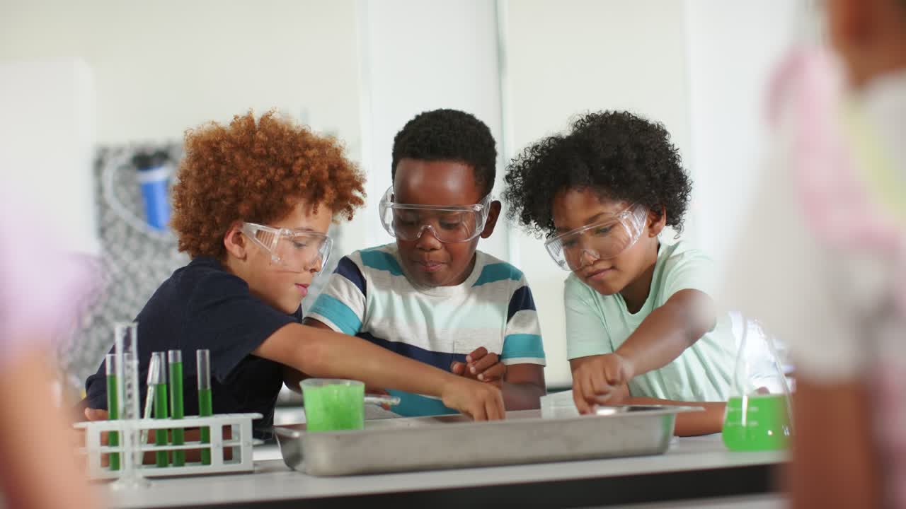 African American preteen boys with goggles checking tubes, pipetting into tray in lab watching mix