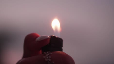 modelo de chica con anillo y uñas pintadas encendiendo un encendedor en una habitación oscura de crepúsculo