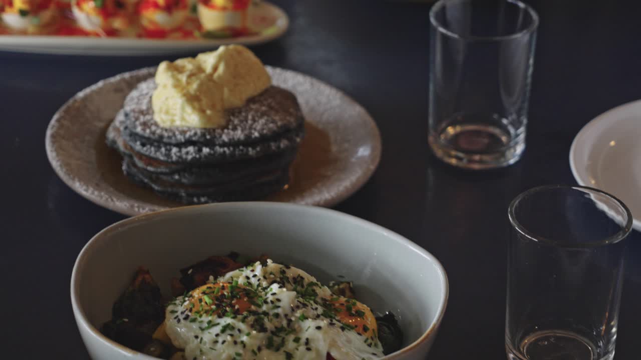 Filmato in slow motion 4K con panoramica di un'elegante tavola da brunch con uova ripiene, insalata, uova all'occhio di bue e pancake guarniti con burro e panna montata.