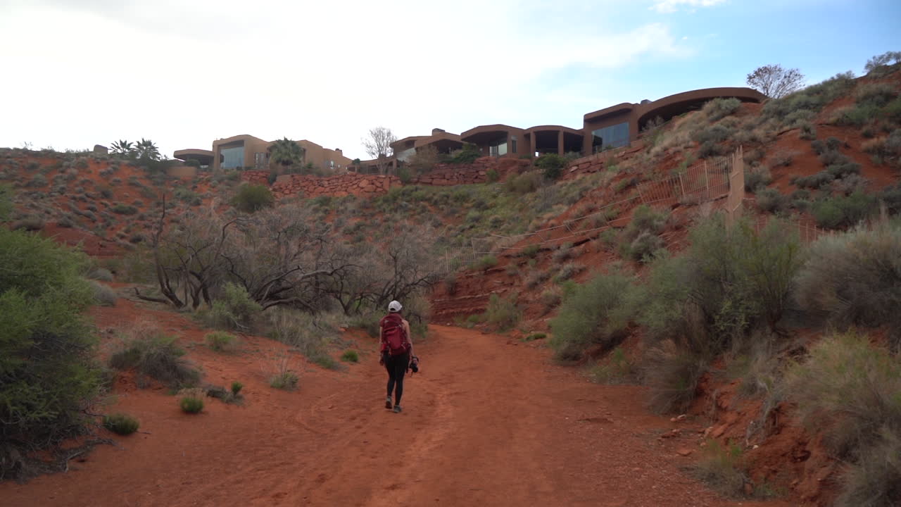 vista trasera de una mujer con una mochila en un sendero de senderismo bajo casas modernas en el paisaje desértico de utah, estados unidos