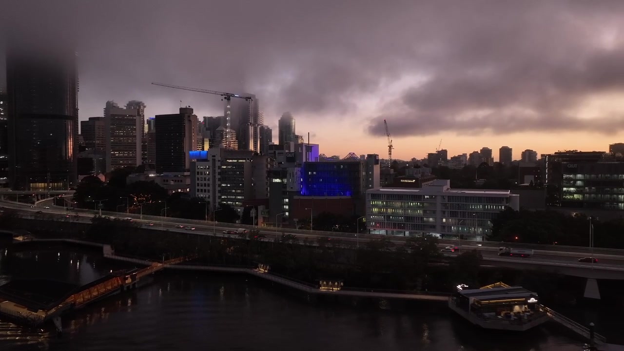 Drone shot orbiting QUT Gardens Point Campus at Sunrise. With low clouds fog covering Brisbane City sky scrapers. Camera slowing tracking towards QUT building. Queensland University of Technology.