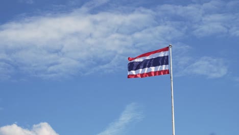 Waving-the-Kingdom-of-Thailand-flag-on-a-pole-with-blue-sky-and-white-clouds-in-the-background