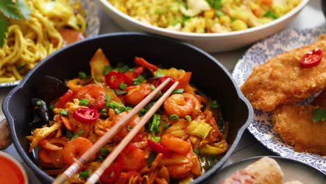 comida asiática servida platos sartenes y tazones llenos de fideos pollo salteado y verduras