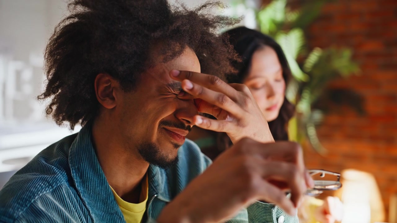 Close up man rubbing eyes taking off glasses. Multiracial startup coworkers.
