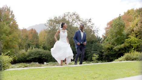 Happy-african-american-bride-and-groom-jumping-and-embracing-at-their-wedding-in-garden,-slow-motion