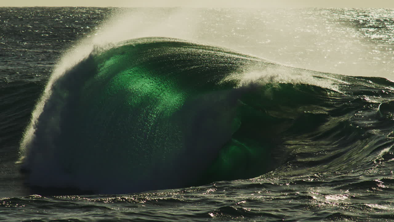 Sunlight strikes rising crest at golden hour, warm glow flickers off surface in isolation