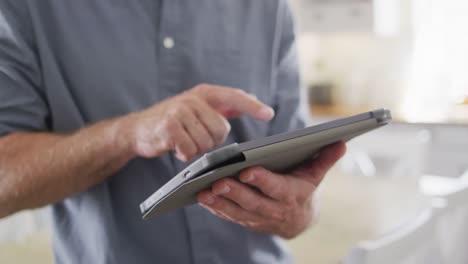 Mid-section-of-caucasian-man-standing-in-kitchen,-using-tablet