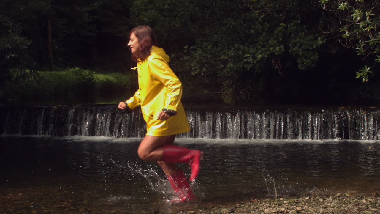 mujer con abrigo de lluvia amarillo corriendo por el agua