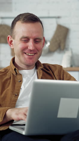 young man freelancer using laptop in the kitchen. happy man having a conversation through the laptop. online working from home. remote work from home during coronavirus quarantine. vertical video