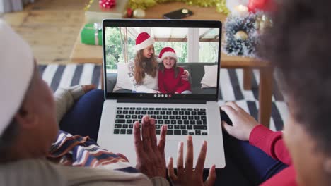 African-american-mother-and-daughter-using-laptop-for-christmas-video-call-with-family-on-screen