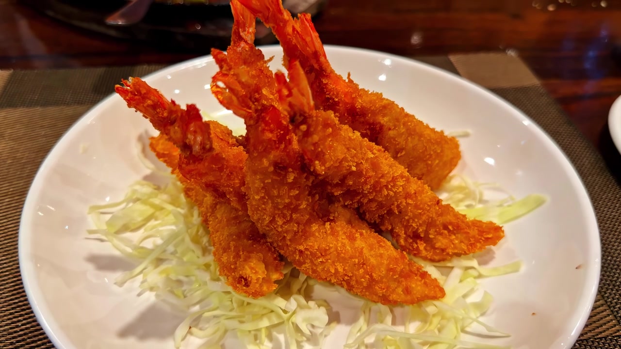 Vista aproximada de camarões crocantes fritos servidos sobre repolho desfiado em um prato branco, provavelmente em um restaurante na Baía de Sogod, Filipinas.