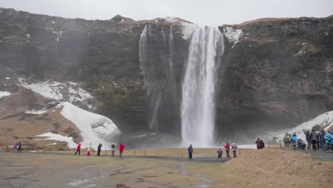 toma estática, en cámara lenta, de muchas personas paradas frente y disfrutando de la vista de la cascada seljalandfoss, en un día nublado de otoño, en islandia