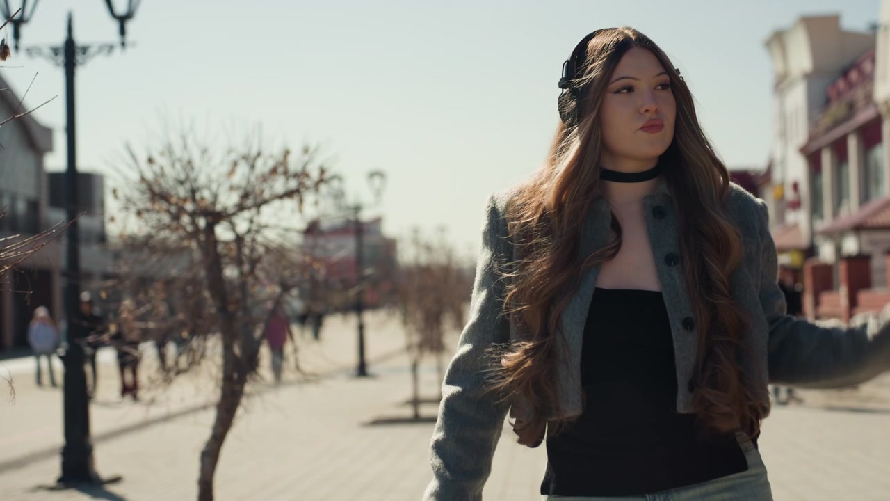 Bella donna asiatica in posa per strada, fashion blogger che sistema capelli e cappotto nella luce dorata, sfondo di un viale fiancheggiato da boutique, sguardo sicuro e atmosfera editoriale, sequenza di stile urbano per i social.