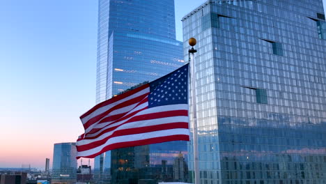 American-flag-waves-at-sunset-against-tall-glass-skyscraper-highrise-buildings