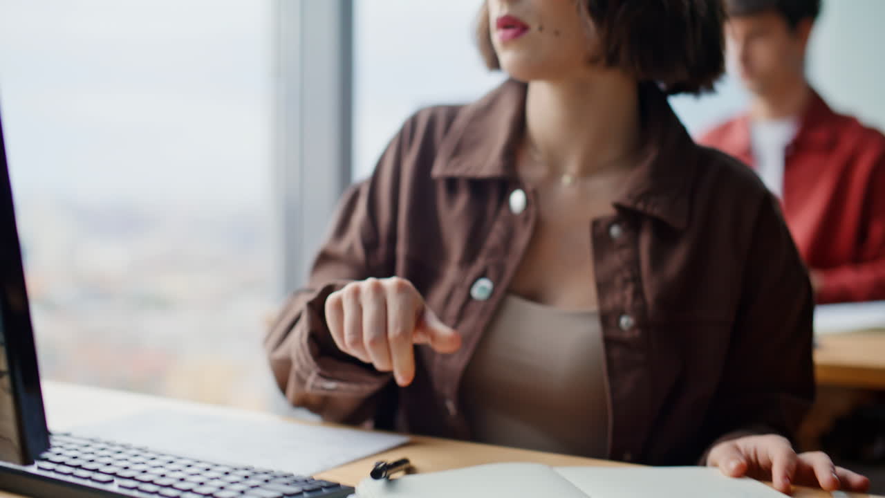 Primo piano di una donna che scrive al computer prendendo appunti in un grande ufficio con finestre