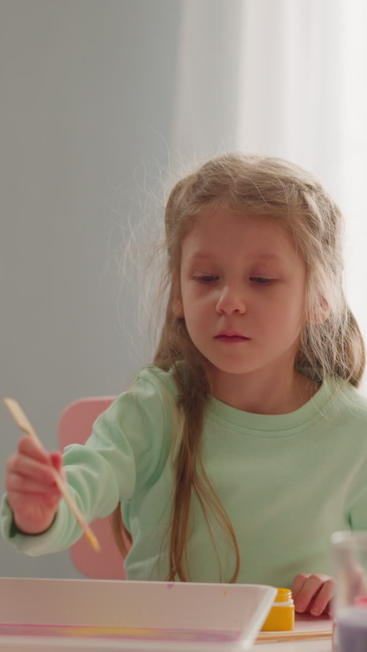 Blonde girl draws with stick on oily water with young teacher at Ebru art masterclass in living room slow motion. Old Turkish design culture practicing