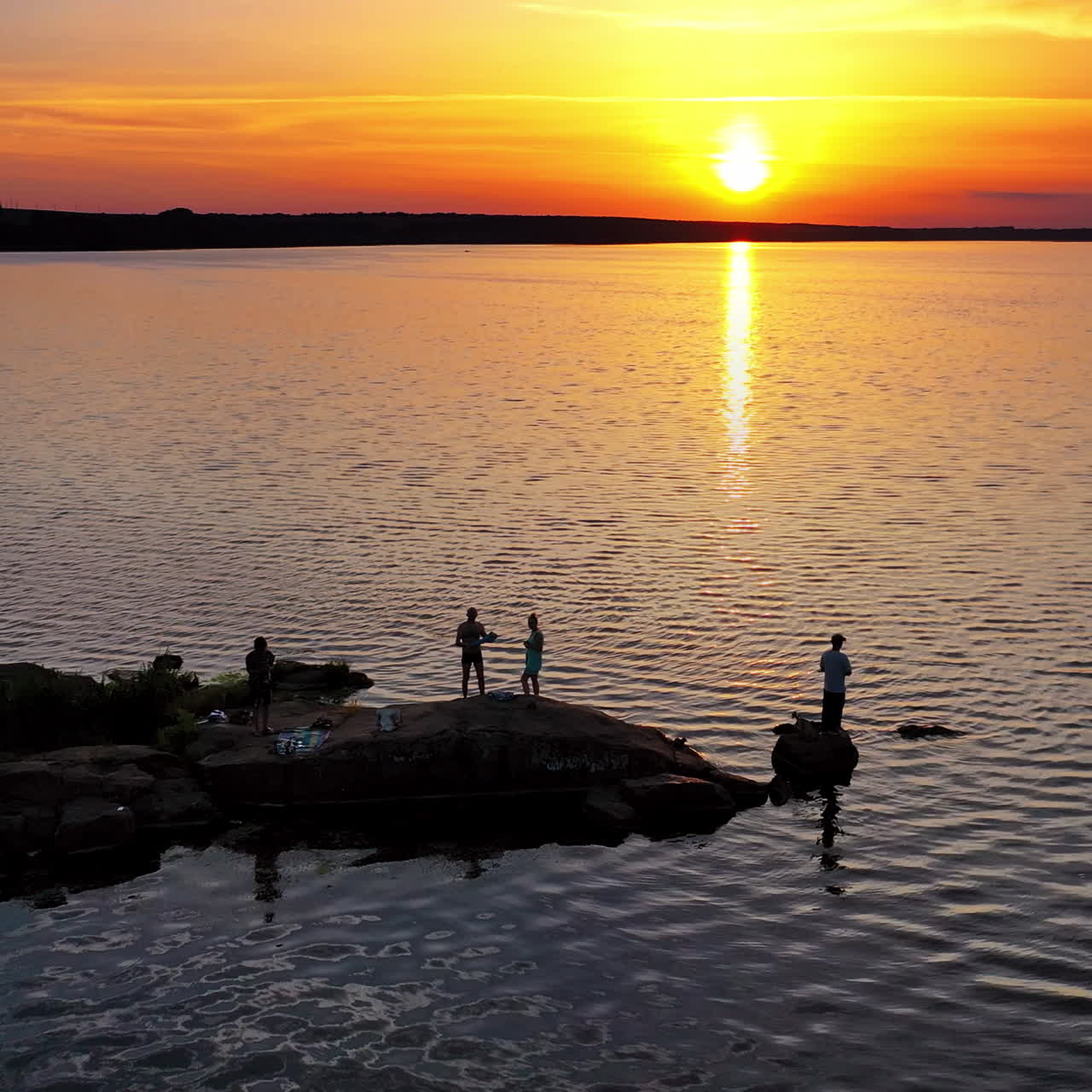 People standing on stones near the water in the evening. Drone view on the natural background of the river and silhouettes of people at sunset. Camera moves up back.