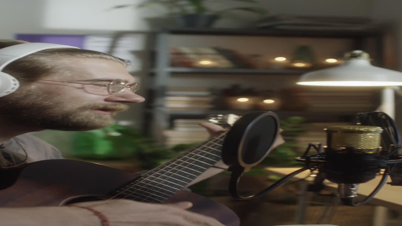 Uomo che suona la chitarra e canta al microfono in studio casalingo
