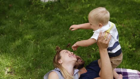 imágenes de ángulo alto de una hermosa familia de tres. acostado en la hierba verde, jugando con su hijo pequeño. estilo de vida feliz. día soleado