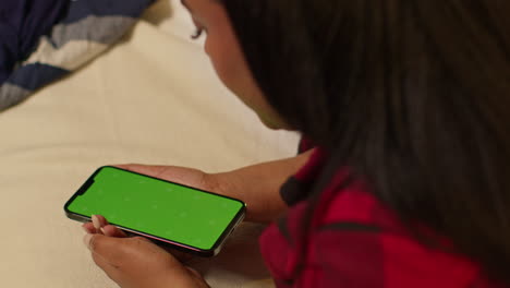 woman lying in bed using phone with green screen