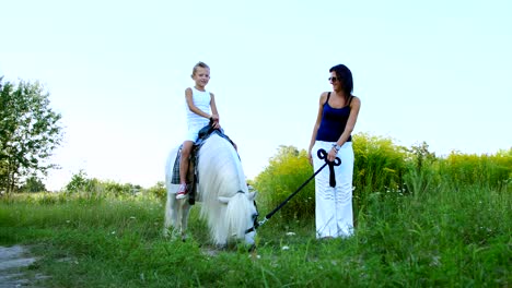 una mujer y un niño están caminando por el campo, el hijo está montando un caballo, la madre está sosteniendo un caballo para una brida. vacaciones familiares alegres y felices. al aire libre, en verano, cerca del bosque