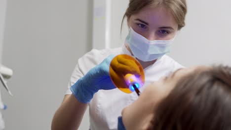 young female dentist in mask and gloves using dental uv light equipment for polymer hardening