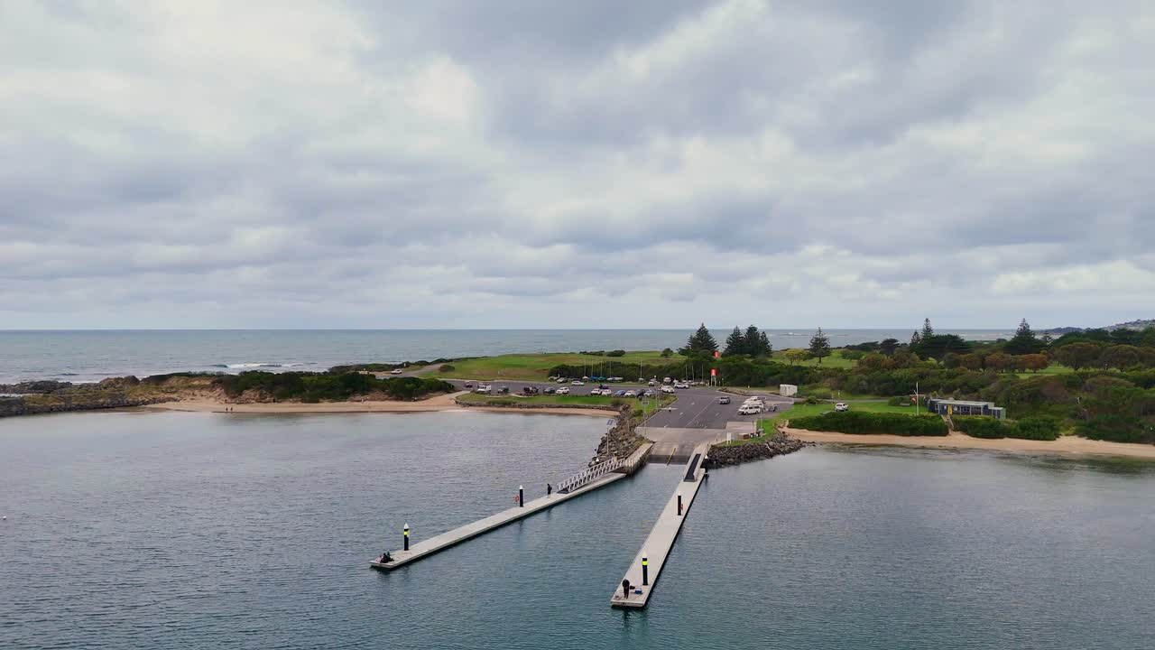 Drone footage captures Apollo Bay's pier, ocean, and lush landscape under overcast skies, highlighting the serene coastal environment
