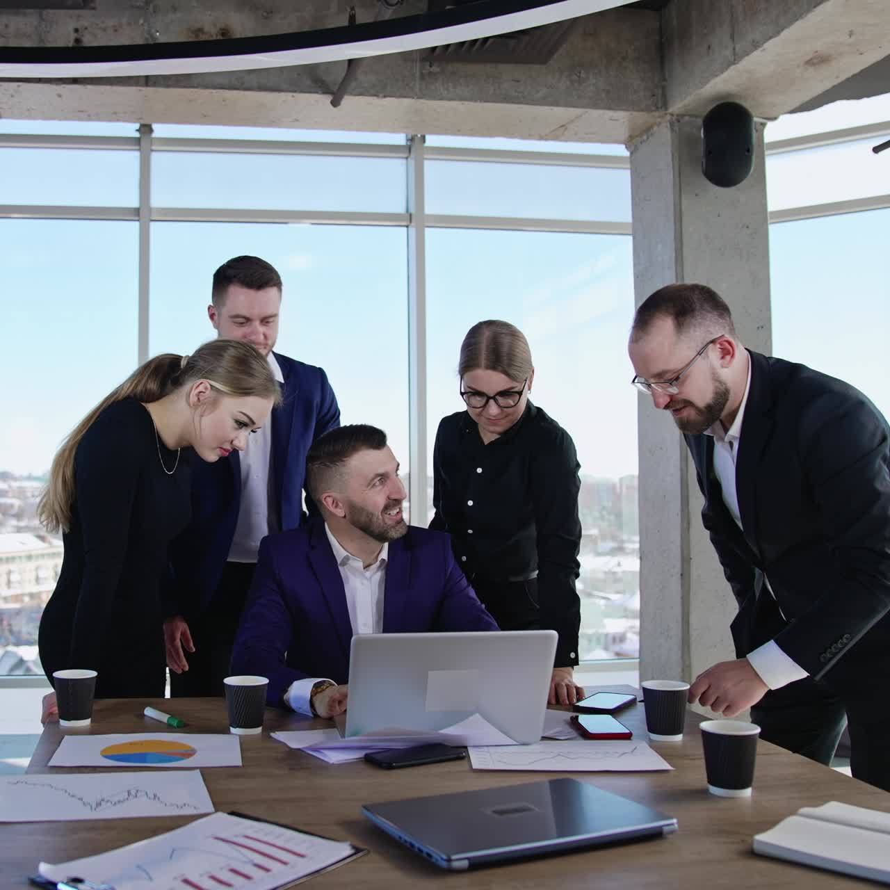 Positive young workmates team brainstorming in office. Man in the centre typing on the computer and smiling. Cityscape at backdrop