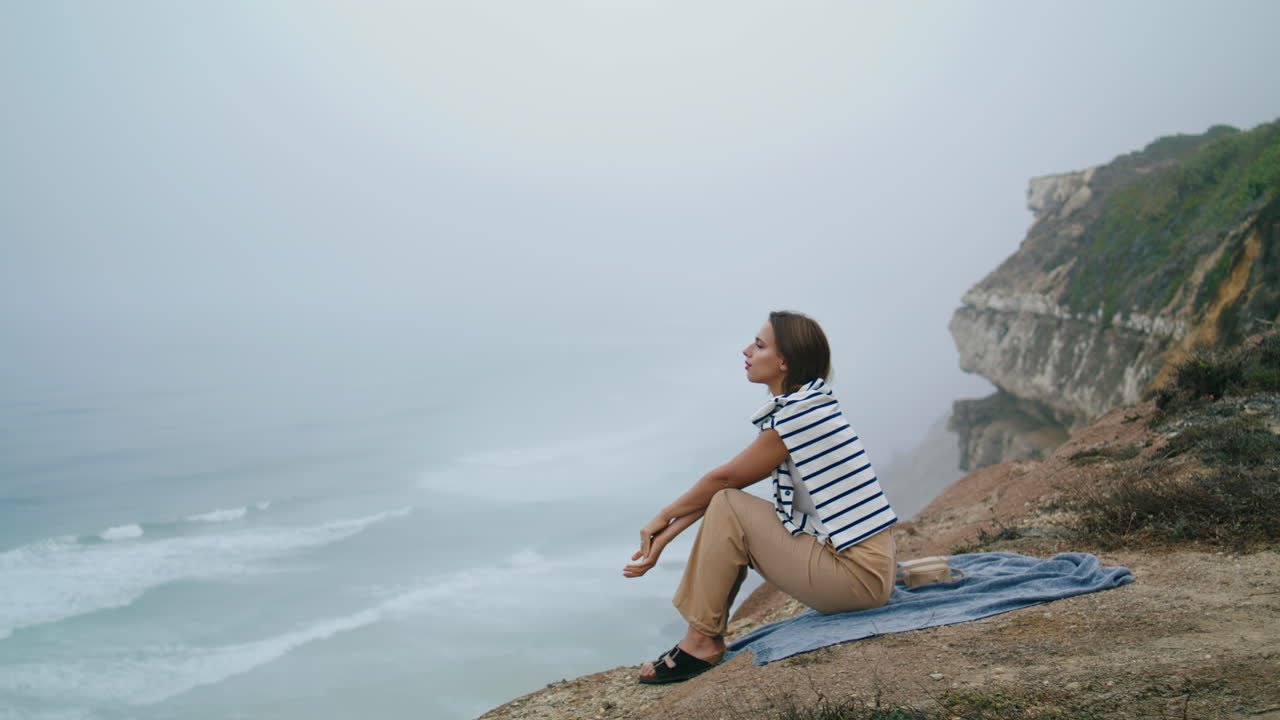 niña pensando relajándose acantilado del océano vertical. mujer serena disfrutando de las olas de la costa