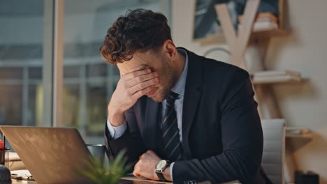 frustrated worker hiding face in palm working laptop in office tired closeup