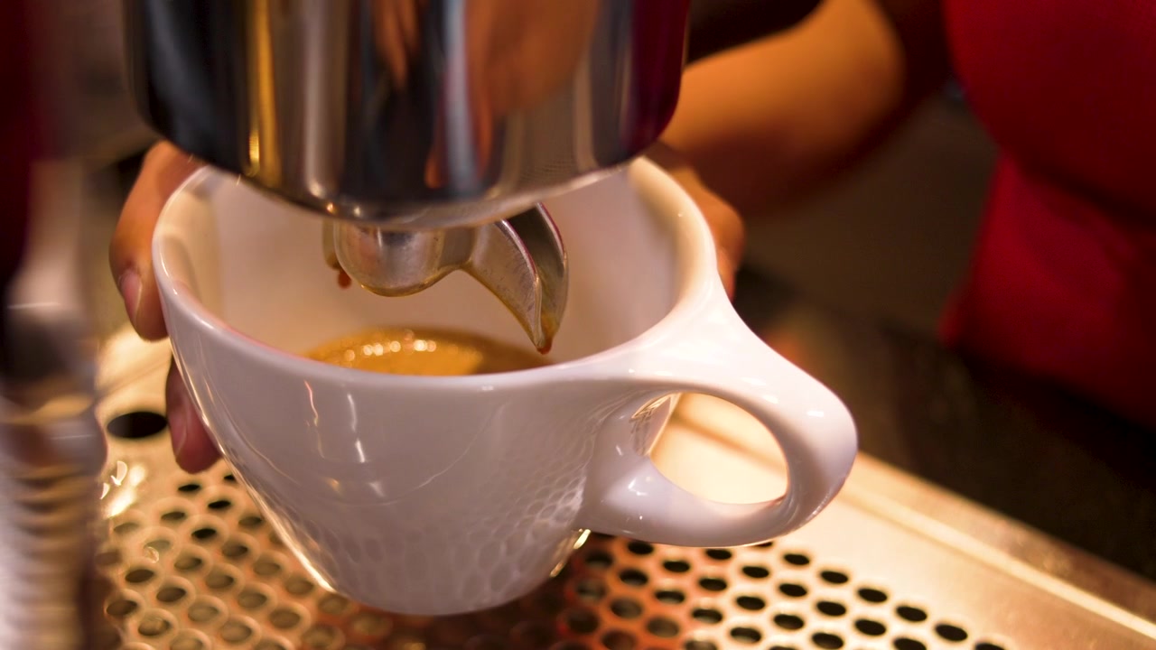 Estrazione di espresso fresco direttamente in una grande tazza di ceramica bianca da una macchina da caffè professionale. Primo piano dell'azione di preparazione del barista in una caffetteria specializzata.
