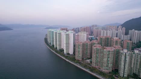 tall colored apartment buildings with blue glass on ma on shan in hong kong just after sunset as the bright white moon shines in the sky in the background