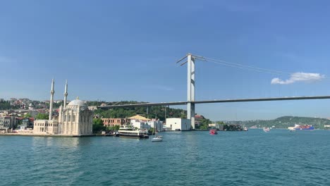 footage of boats passing on bosphorus, historical landmark called "ortakoy mosque" and bridge in istanbul. it is a beautiful scene in a sunny summer day.