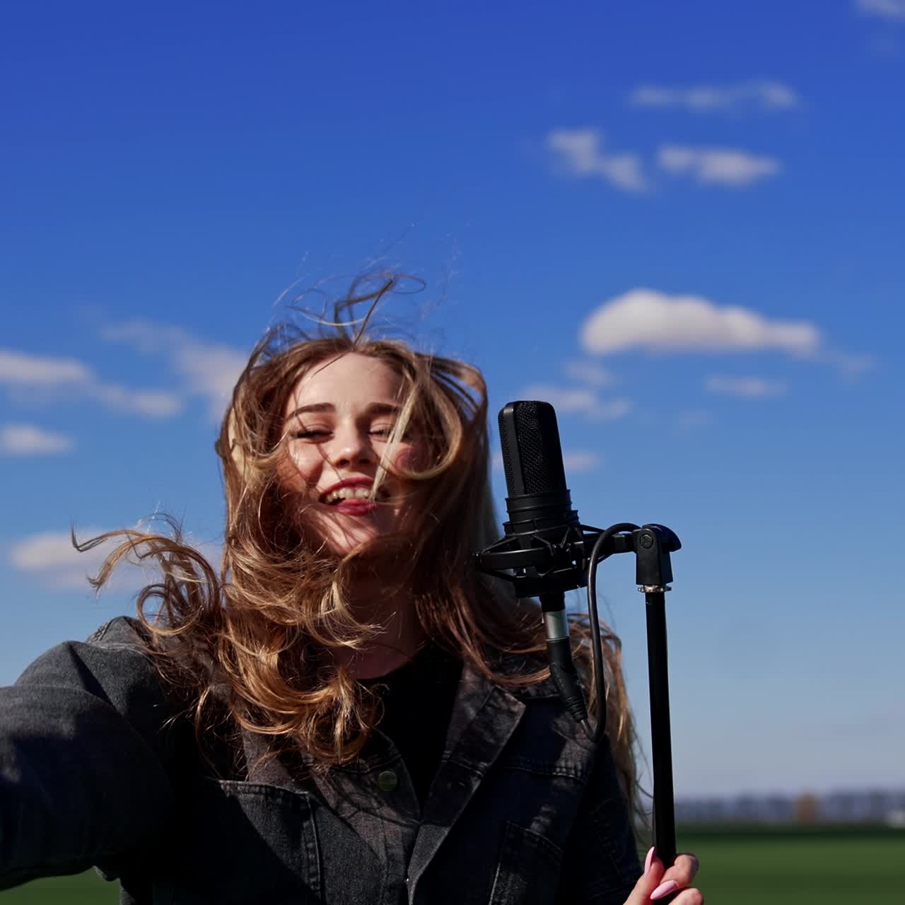 Beautiful singer on blue sky background. Young woman singing and jumping near the microphone while performing concert outdoors