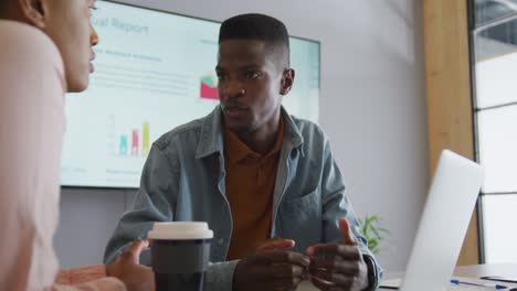 Smiling-african-american-male-and-female-colleague-in-discussion-at-meeting-using-laptop-and-screen