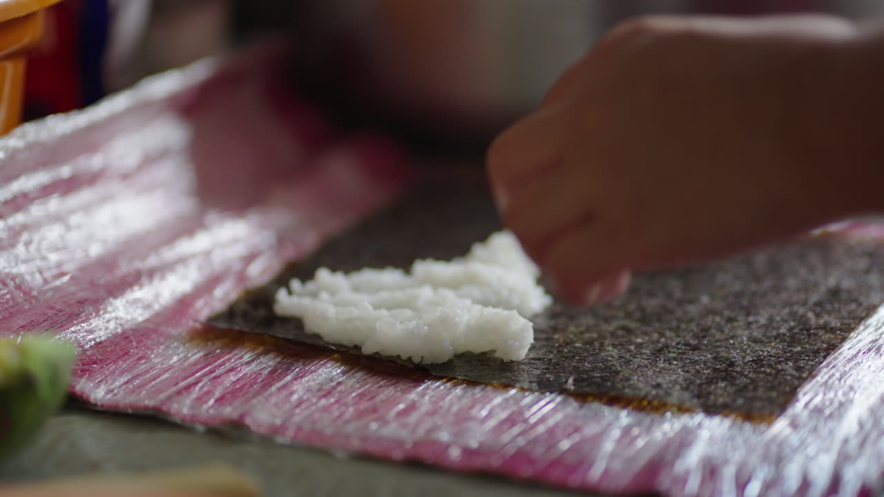 Close-up of hands pressing rice onto nori seaweed for sushi preparation on cutting board in natural kitchen light