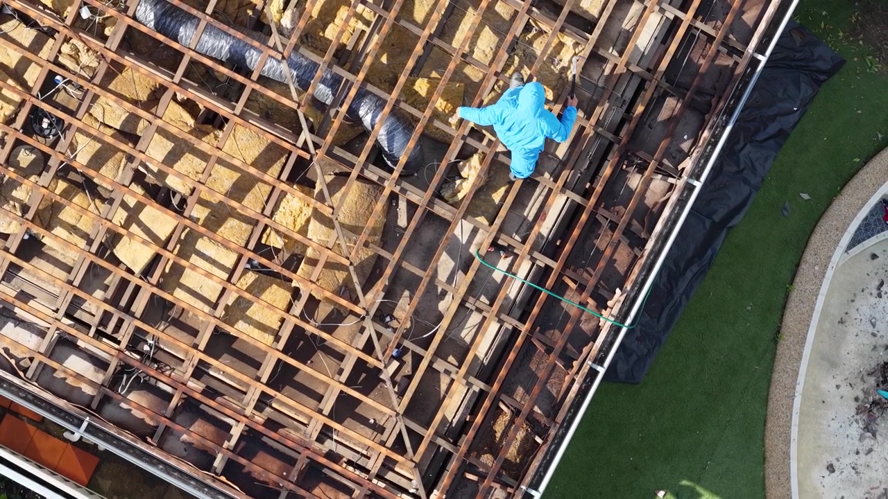 Worker in Protective Suit Removing Old Roof Insulation