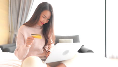 young pretty asian woman shopping online, using laptop computer and bank credit card, full frame