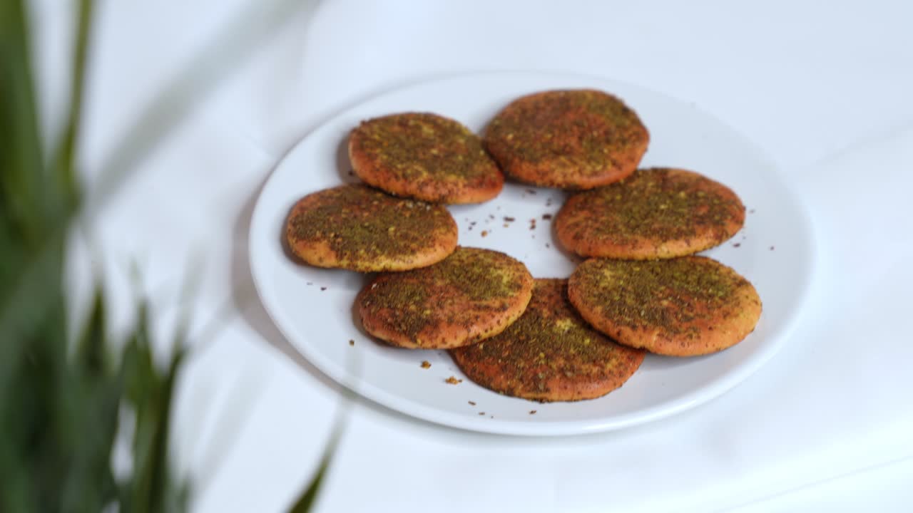 A close-up of a woman’s hand with polished nails picking a golden zaatar cookie from a plate. 4K quality, perfect for Middle Eastern food, lifestyle, or culinary content.