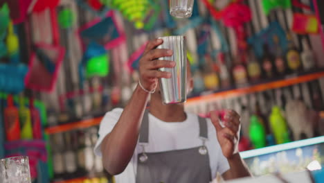 barman takes shaker and glass in club. concentrated bartender does tricks with cocktail equipment in bar. african american man works at counter