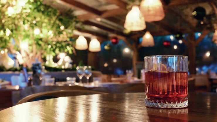 Bicchiere di cocktail rosso su un tavolo di legno all'interno di un ristorante con illuminazione calda