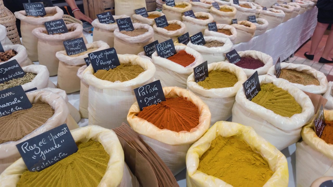 Close view of large bags of colorful spices with handwritten French price labels at a market stall, Cannes, France