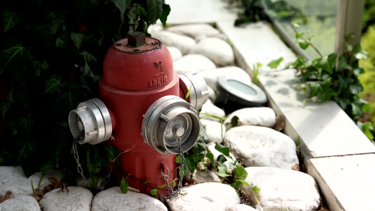 Idrante antincendio esterno rosso circondato da sassi di fiume bianchi, luce a terra e foglie d'edera