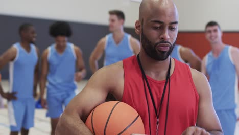 Porträt-Eines-Gemischtrassigen-Männlichen-Basketballtrainers-Auf-Dem-Hallenplatz-Mit-Einer-Vielfältigen-Männlichen-Mannschaft,-In-Zeitlupe