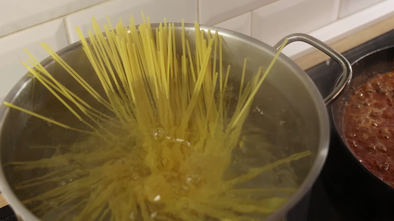 Spaghetti che cadono artisticamente in acqua bollente all'interno di una pentola di metallo durante la cottura.