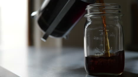 woman pours coffee from french press into mason jar