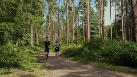 mid adult couple exercising doing work out outdoors running along track through forest towards camera wearing sports clothing shot in real time 1